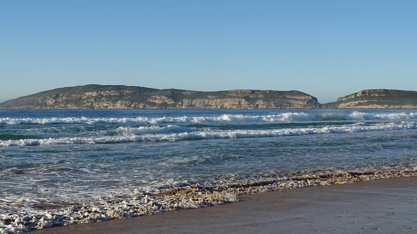 Waves breaking on a Plettenberg Bay beach with the Robberg peninsula lying across the bay